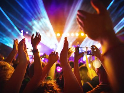 Rear view of excited crowd enjoying a DJ performance at a festival. There are many raised hands, some of the holding cell phones and taping the show.
People in foreground are released.