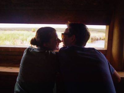Happy young couple bird watching in wooden hut in Africa, back lit by sunset.