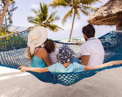 Rear view of parents and their small kids relaxing in hammock during summer day on the beach.