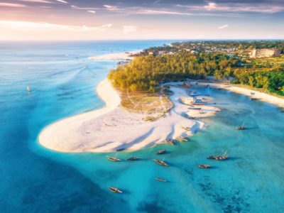 zanzibar. Aerial view of the fishing boats on tropical sea coast with sandy beach at sunset. Summer travel in Zanzibar, Africa. Top view of boats, yachts, green palm trees, clear blue water, colorful sky