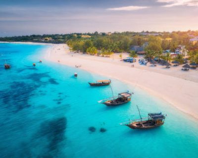 zanzibar.. Aerial view of the fishing boats on tropical sea coast with white sandy beach at sunset. Summer holiday on Indian Ocean, Zanzibar. Landscape with boat, palm trees, transparent blue water. Top view