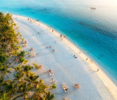 Zanzibar white sand beach Aerial view of green palm trees, umbrellas on the sandy beach of Indian Ocean at sunset. Summer holiday in Kendwa, Zanzibar island. Tropical landscape with palms, white sand, clear blue sea. Top view